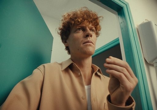 Reference still: a red-haired man in a tan shirt against a saturated teal doorframe, warm skin against cool cyan, softer contrast and lifted blacks